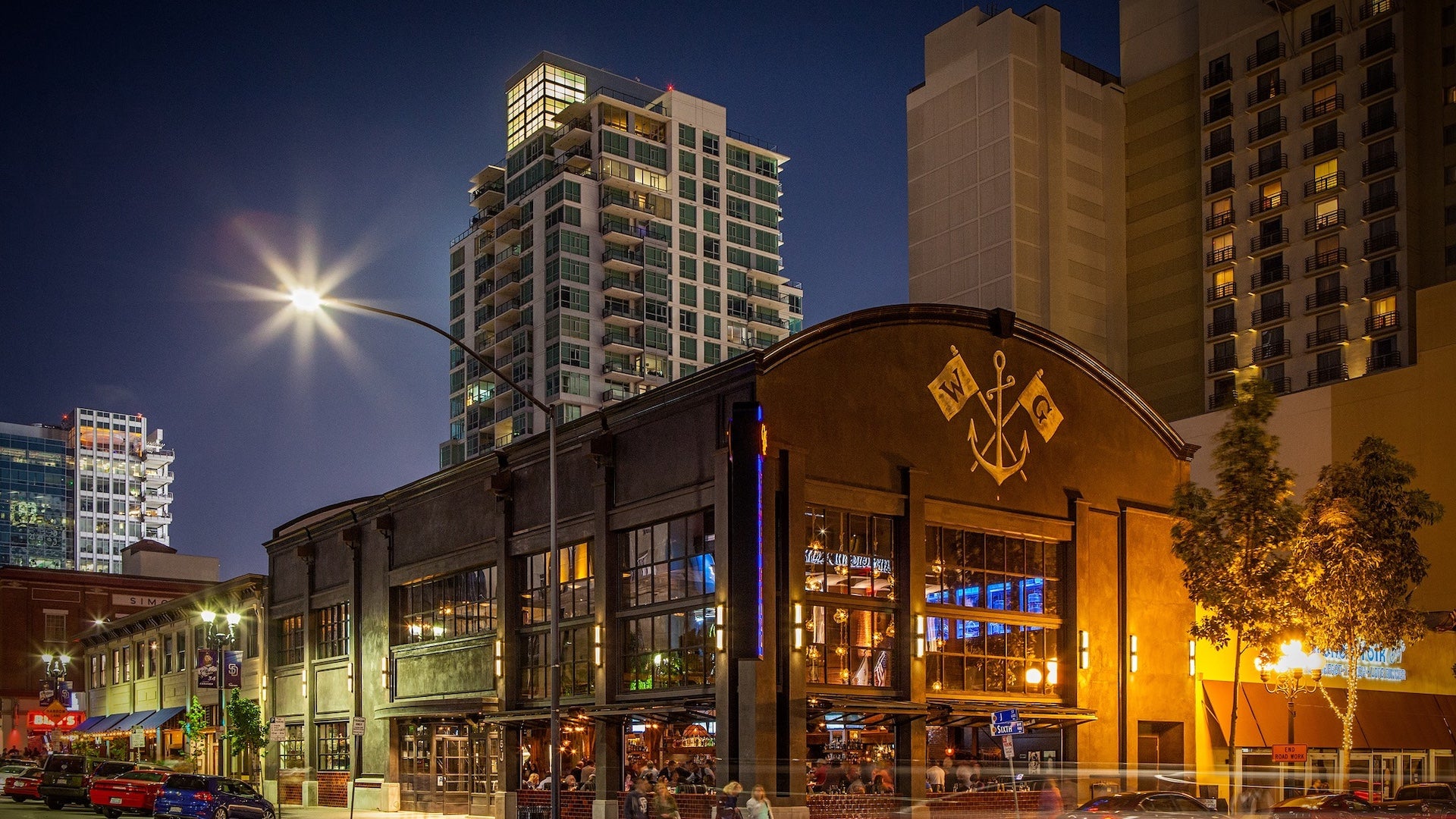 Nighttime view of Water Grill San Diego, a modern seafood restaurant with a rustic facade and large windows, set against a backdrop of high-rise buildings in the Gaslamp Quarter.